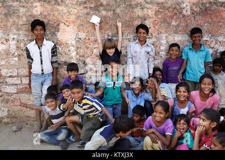 Jungen kaukasischen Jungen mit Bündel von lächelnden indische Kinder umgeben, die Hände, das Dorf in der Nähe von Pushkar, Rajasthan, Indien. Stockfoto