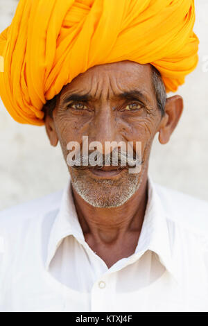 Porträt der alten indischen Mann im weißen Outfit tragen orange Turban, vor der weißen Wand in einem Dorf in der Nähe von Pushkar, Rajasthan, Indien stehen. Stockfoto