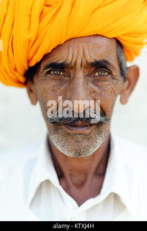 Porträt der alten indischen Mann im weißen Outfit tragen orange Turban, vor der weißen Wand in einem Dorf in der Nähe von Pushkar, Rajasthan, Indien stehen. Stockfoto