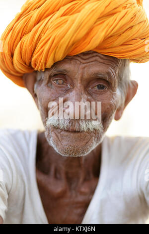 Porträt der alten indischen Mann im weißen Outfit tragen orange Turban, vor der weißen Wand in einem Dorf in der Nähe von Pushkar, Rajasthan, Indien stehen. Stockfoto