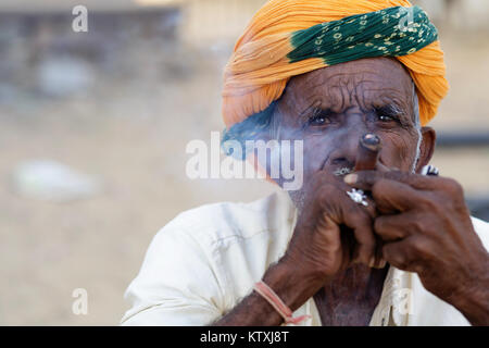 Indische Mann mit der Gelben Turbane rauchen Zigarre, ein traditionelles Dorf in der Nähe von Pushkar, Rajasthan, Indien. Stockfoto