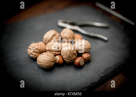 Gemischte ganze Nüsse in der Schale, einschließlich Walnüsse, Haselnüsse, Mandeln und Pekannüsse mit einem Nussknacker Stockfoto