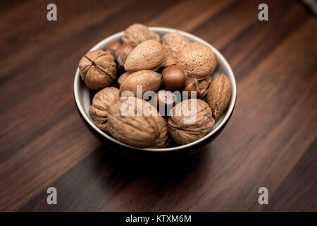 Eine Schüssel gemischten ganze Nüsse in der Schale, einschließlich Walnüsse, Haselnüsse, Mandeln und Pekannüsse mit eine kurze Schärfentiefe Stockfoto