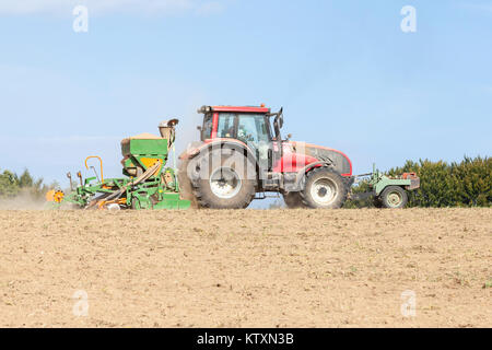 Bauer Pflanzen und Säen eine Frühling-ernte mit Traktor und Amazone Sämaschine in einem brachliegenden Feld in einer Nahaufnahme Seite Blick auf die Skyline mit Kopie spac Stockfoto