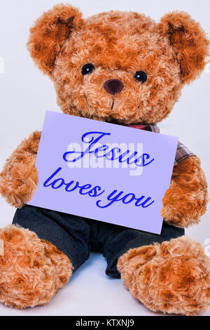 Cute teddy bear Holding ein violettes Schild mit der Aufschrift Jesus liebt Dich auf weißem Hintergrund Stockfoto