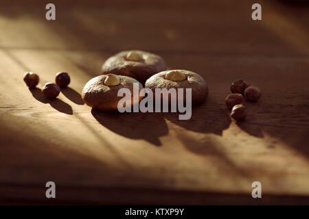 Gesundes zuhause - Haselnuss butter Cookies mit Haselnüssen auf rustikalen braunes Holz Tisch leuchtet mit dramatischen Sonnenlicht, künstlerische food Still Life Stockfoto