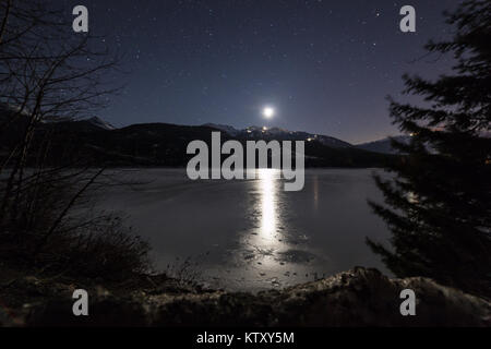 Mond reflektierte Licht auf einem zugefrorenen See mit Schnee Berge im Hintergrund gekrönt Stockfoto