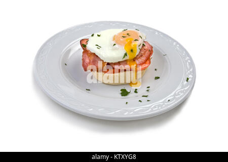 Weiche pochiertes Ei auf Muffin mit Schinken und Tomaten auf weißem Hintergrund Stockfoto