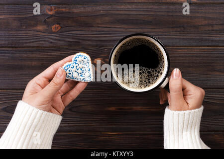 Weibliche Hände mit Kaffee und herzförmige Plätzchen auf Holztisch, Ansicht von oben. Stockfoto