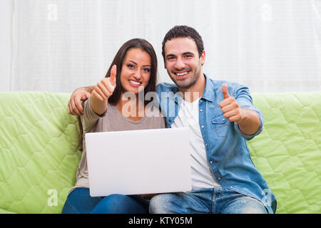 Glückliches Paar auf dem Sofa zu Hause sitzen und mit Laptop. Stockfoto