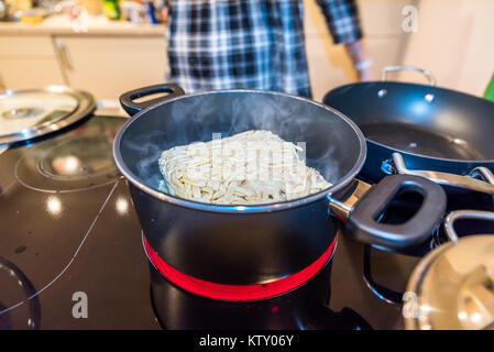 Brick gefrorene Nudeln im Pan-Auflauf mit kochendem Wasser auf modernen Elektroherd. Stockfoto