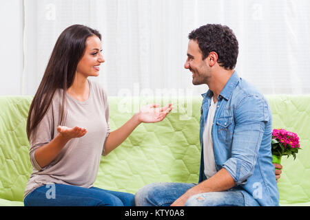 Junges Paar sitzt auf einem Sofa zu Hause. Mann will Blumen für seine Frau zu geben. Stockfoto