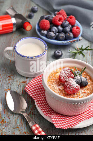 Crème Brûlée mit Himbeeren, Heidelbeeren und Rosmarin in Weiß ramekin mit Zutaten und brennende Fackel auf rustikalen Holztisch. Stockfoto