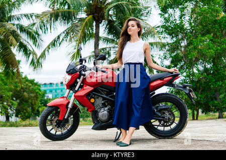 Frau standng in der Nähe von ihr Motorrad auf Palm Background Stockfoto