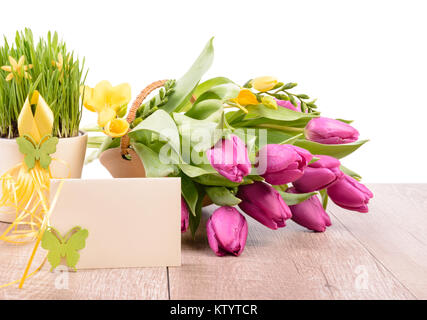 Spring Flower Arrangement und eine Grußkarte an einem hölzernen Tisch gegen weiße Wand, text Raum Stockfoto