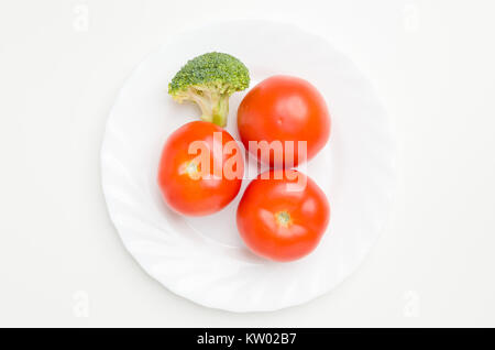 Ansicht von oben flach von drei frische Tomaten und frischem Brokkoli Stück auf weiße Platte auf weißem Hintergrund. Stockfoto