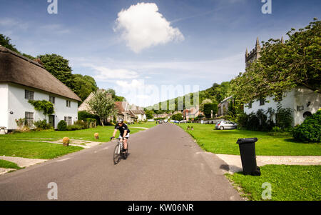 Dorchester, England, Großbritannien - 8 August, 2013: ein Radfahrer kommt herab, der Hauptstraße der malerischen Dorf Milton Abbas, gesäumt mit traditionellen strohgedeckten Stockfoto