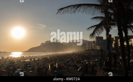 Die Sonne ist absteigend am Strand in Rio de Janeiro. Der Strand ist mit Menschen warten auf einen atemberaubenden Sonnenuntergang überfüllt. Es gibt silhoettes der Palme Stockfoto