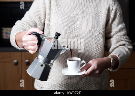 Ein smart, aber leger gekleidete Frau gießen einen Espresso aus einer moka Herd Espressomaschine während Stehen in Ihrer Küche zu Hause. Stockfoto