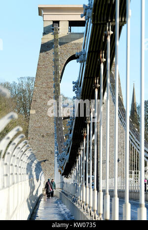 Eine Frau, die eine große Tasche, die über die Clifton Suspension Bridge in Bristol, UK. Ein kalter Wintertag und es gibt Eis und Schnee auf dem Gehweg. Stockfoto