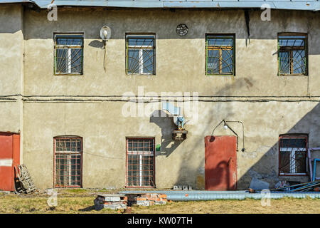 Die Fassade eines alten Hauses mit Fenstern und Türen, Müll Gebäude im Hof an einem hellen, sonnigen Tag. Stockfoto