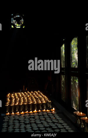 Kerze Zimmer in einem buddhistischen Kloster: Reihen von tibetischen Öllampen brennen in der Dunkelheit, Lichtstrahlen fallen aus dem Fenster. Stockfoto