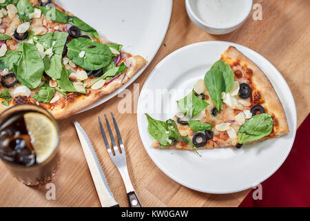 Frische Pizza mit Spinat, Mandeln, Oliven und Parmesan auf hölzernen Tisch im Restaurant. Stockfoto