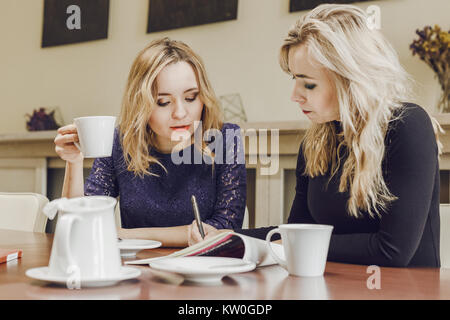 Zwei junge Frauen diskutieren, Dokumente und Tee trinken bei der Sitzung im Konferenzraum Stockfoto