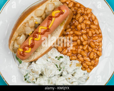 Hot Dog in einem Brötchen mit Baked Beans und Kartoffelsalat auf blauem Grund Stockfoto