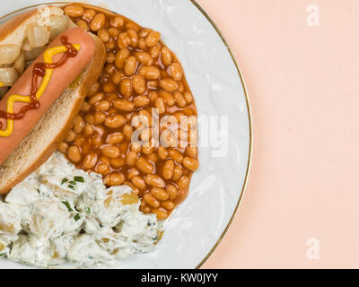 Hot Dog in einem Brötchen mit Baked Beans und Kartoffelsalat blass Orange Hintergrund Stockfoto