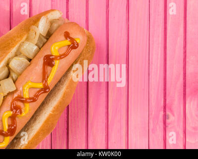 Hot Dog in einem Brötchen mit gebratene Zwiebel Ketchup und Senf vor einem rosa Hintergrund Stockfoto