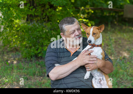 Älterer Mann mit seinem niedlichen Hund (Basenji), die es in den Händen, während er im Sommer park Bärtigen Stockfoto