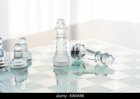 Eine klare und satiniertem Glas Schach Spiel gerade beendet. Der König steht, während die anderen in der Niederlage legt. Der Hintergrund ist weiß. Stockfoto