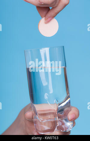 Vitamine, Gesundheit, Medikamente. Person werfen Vitamin Mineral ergänzen Brausetablette in einem Glas Wasser. Studio gedreht auf blauem Hintergrund Stockfoto