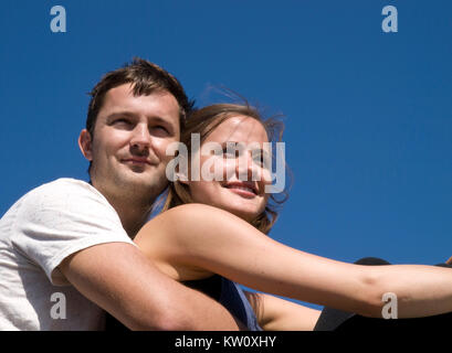 Attraktive junge Paar Lächeln eng zusammen mit der Waffe des Mannes um die Frau in die Ferne vor blauem Himmel Hintergrund Stockfoto