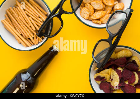 Ein Abend mit Freunden vor dem Fernseher. Drei Schalen mit salzigem Brot Sticks, Semmelbrösel und Chips, zwei Gläser und eine Flasche kalten Sto Stockfoto