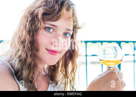 Closeup Porträt einer Glücklich lächelnde junge Frau mit Bourbon rum alkoholische Getränk in der Hand durch Wasser im Sommer Restaurant Stockfoto