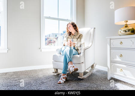 Helles, weißes, modernes Schaukelstuhl im Kinderzimmer mit Kommode, Dekorationen in Modell staging Haus, Wohnung oder Haus, eine junge Frau sittin Stockfoto