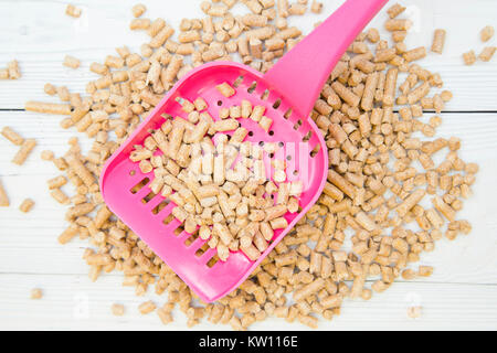 Pet Care Concept. Ein rosa Wurf Schaufel mit Wurf Füllstoff für Nagetiere, Hasen und Katzen auf einem weißen Holz- Hintergrund, aus der Nähe. Raum für Ihre Text- oder im Stockfoto