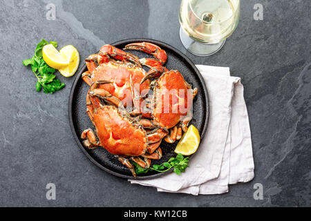 Gekochte Krabben auf dem schwarzen Schild mit weißem Wein serviert, schwarzer Schiefer Hintergrund, Ansicht von oben. Stockfoto