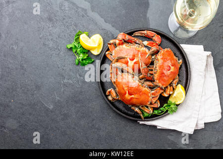 Gekochte Krabben auf dem schwarzen Schild mit weißem Wein serviert, schwarzer Schiefer Hintergrund, Ansicht von oben. Stockfoto