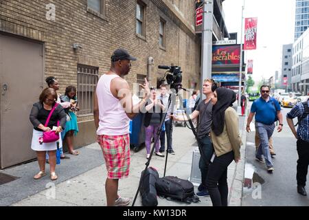 Bevor eine Leistung der Broadway Musical Hamilton zwei Tage vor dem Schöpfer Lin Manuel Miranda aus der Show, eine TV-Crew Interviews ein Mann während Touristen pass auf 46th Street, New York City, New York, 7. Juli 2016. Stockfoto