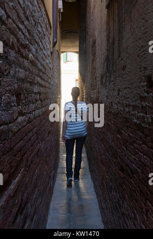 Ein Tourist zu Fuß in eine schmale Gasse zwischen den Gebäuden in Venedig Stockfoto