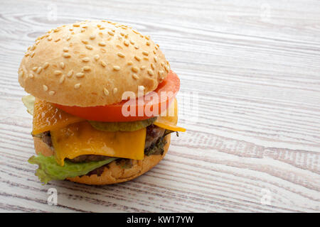Hamburger mit Käse, Fleisch, Tomaten, Zwiebeln und Kräutern. Auf hölzernen Hintergrund. Stockfoto