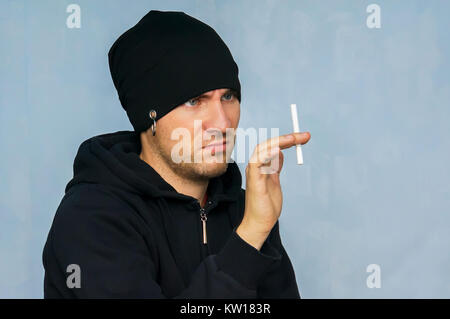 Ein junger Mann in der Subkultur Jugend Kleidung halten einer Zigarette. Durch Rauchen angewidert. Mit dem Rauchen aufzuhören. Abneigung gegen Tabak rauchen. Der Kampf gegen die Smok Stockfoto