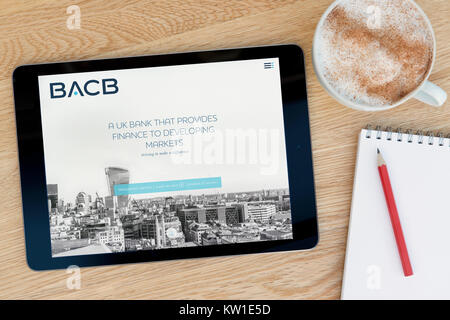 Der bacb (British Arab Commercial Bank) Website auf einem iPad, ruht auf einem hölzernen Tisch neben einem Notizblock, Bleistift und Tasse Kaffee (nur redaktionelle Nutzung). Stockfoto