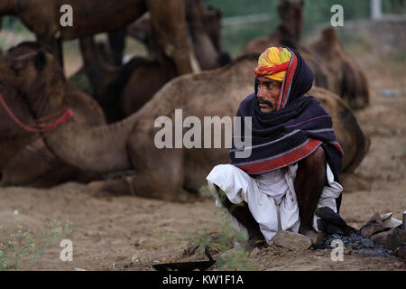 Szene in Pushkar Camel Fair, Mann mit der Gelben Turbane mit Decke bedeckt, sitzt von gelöscht Kamin, Ajmer, Pushkar, Rajasthan, Indien Stockfoto