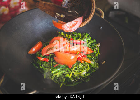 Hinzufügen von rot in Scheiben geschnittenen Tomaten in Wasser Spinat rühren braten, Nahaufnahme Stockfoto