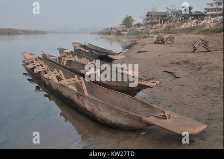 River Bank mit langen hölzernen Kanus im Vordergrund, im Hintergrund das Dorf, das klare Wasser des Flusses, Chitwan, Nepal. Stockfoto