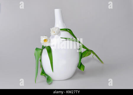 Zwei Weiße Tulpen auf langen grünen Stengel liegen auf runde weiße Vase und schauen sich an, sich zu verlieben. Stockfoto